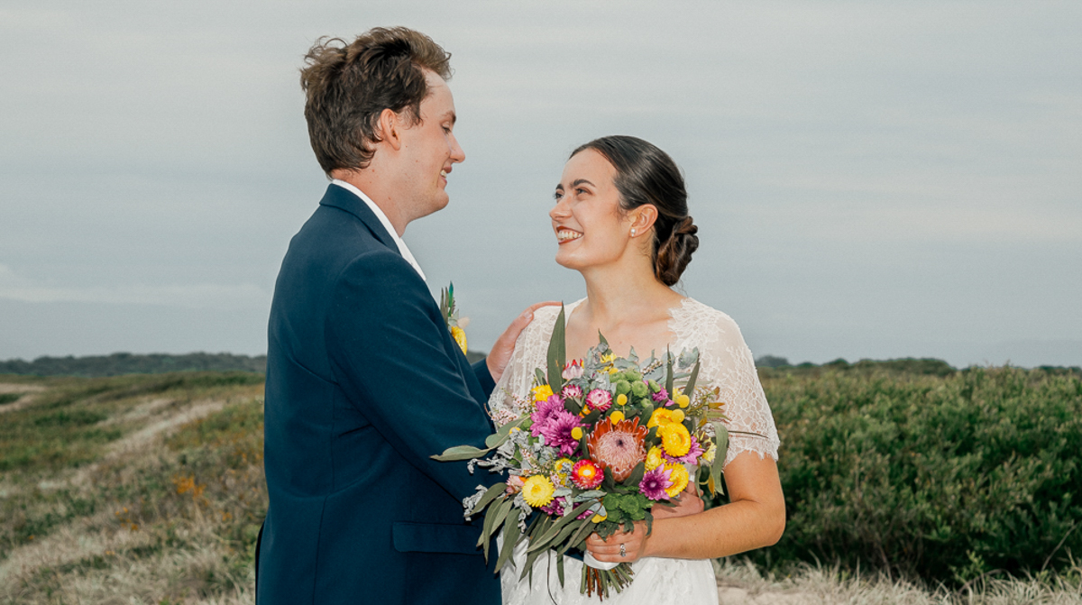 The bride and groom are embracing and looking into one another's eyes while the bride holds a beautiful bright bundle of flowers photographed by Olivia Holley Studio